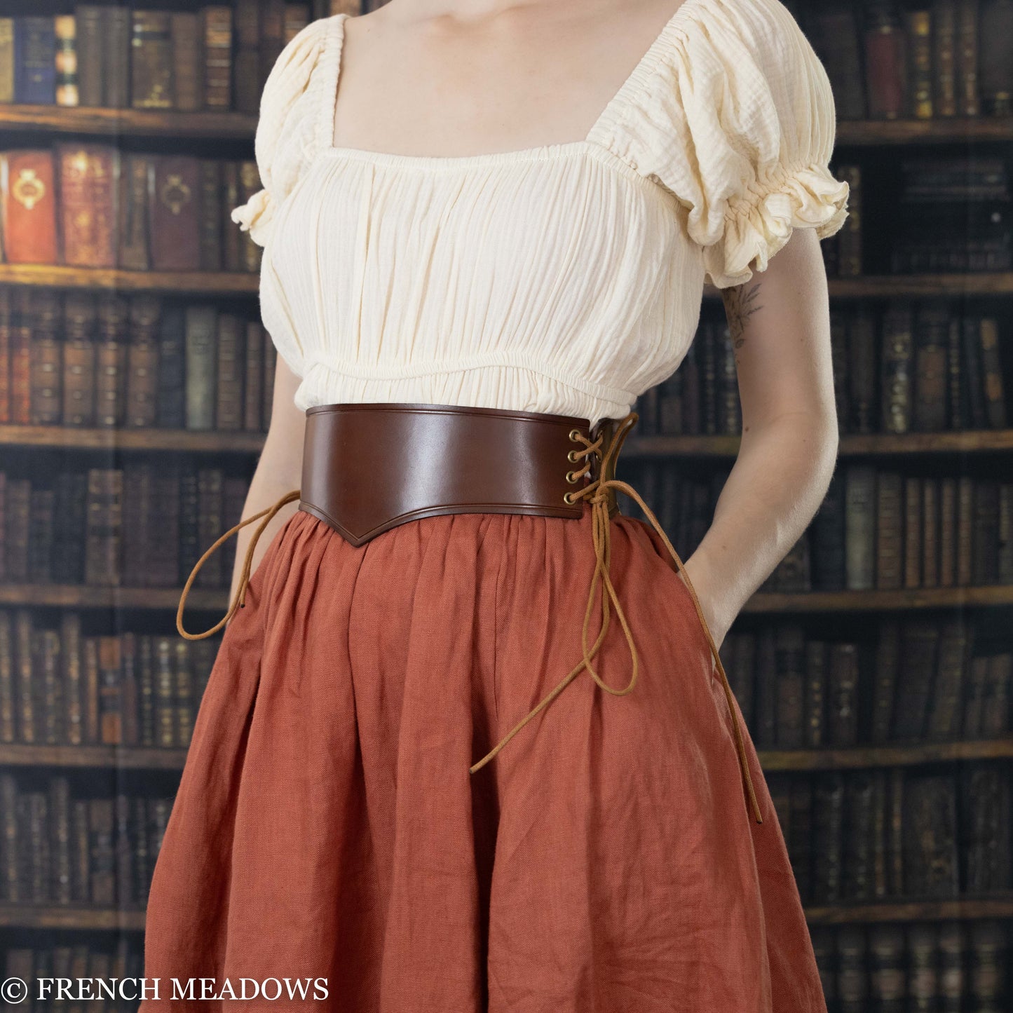 model wearing brown leather waist harness over cream colored dress and orange linen renaissance skirt