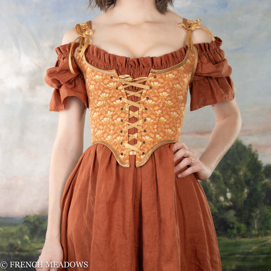 model wearing an orange floral corset over a dark orange linen dress, creating a corset dress look