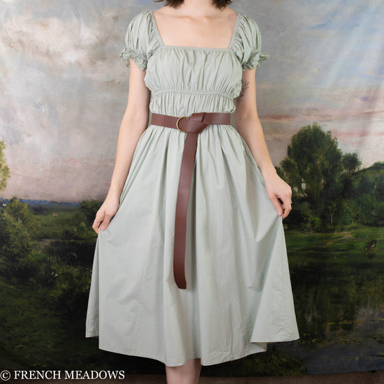 modeling wearing light pistachio colored dress with a leather O-ring belt belted at the waist