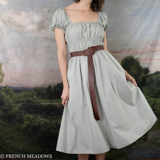 Load image into Gallery viewer, modeling wearing light pistachio colored dress with a leather O-ring belt belted at the waist and twirling to the side to show the volume of the skirt
